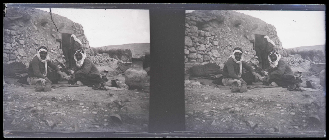 Hommes assis devant une habitation en pierre et en terre.