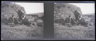 Hommes assis devant une habitation en pierre et en terre.
