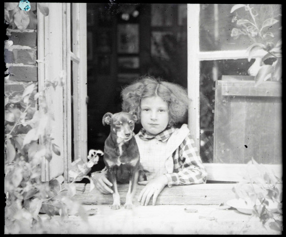 Portrait d'une petite fille et un petit chien à une fenêtre. (famille Bretocq).