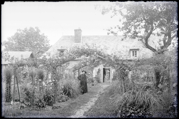 Curé dans un jardin devant une maison de la campagne normande.