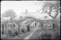 Curé dans un jardin devant une maison de la campagne normande.
