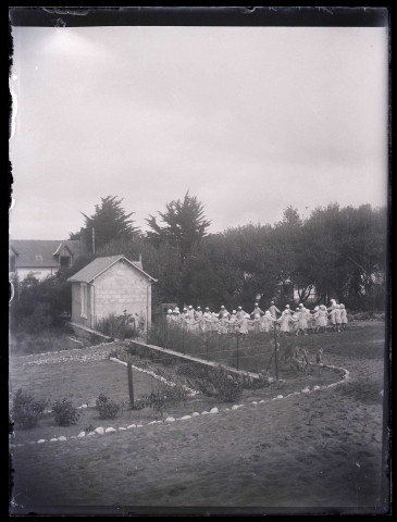 Femmes et enfants dansant la farandole dans un jardin.