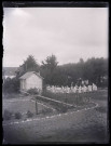 Femmes et enfants dansant la farandole dans un jardin.