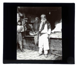 Homme en costume traditionnel devant une échoppe.