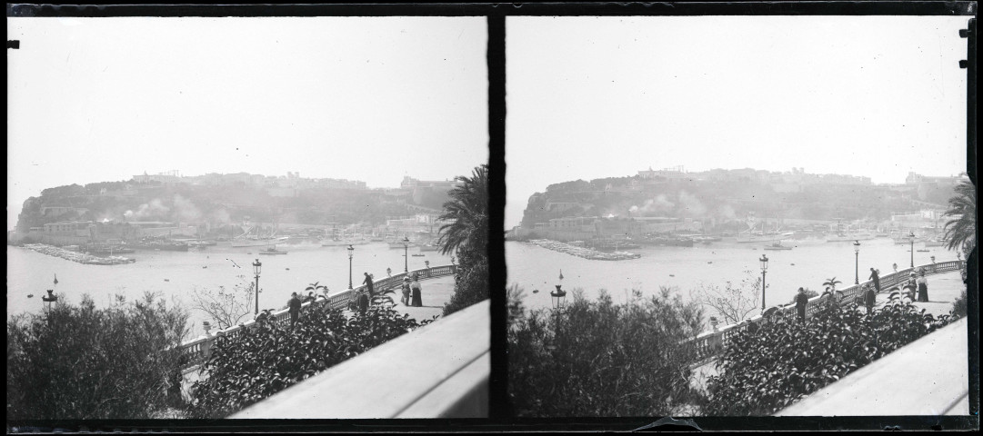 Hommes et femmes se promenant sur un balcon surplombant un port méditerranéen.