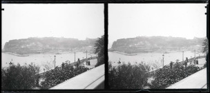 Hommes et femmes se promenant sur un balcon surplombant un port méditerranéen.