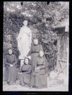 Femmes dans un jardin au pied de la statue d'un saint.