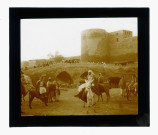 Bédouins sur leur monture devant un pont en pierre donnant accès à une forteresse.