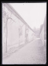 Ruelle bordée par un long bâtiment couvert de vignes.