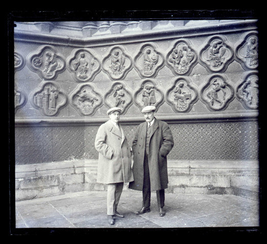 Deux hommes devant les bas-reliefs de soubassement de l'ébrasement côté gauche du portail central de la façade Ouest, dit Portail du Saint-Sauveur, de la Cathédrale d'Amiens (Somme)