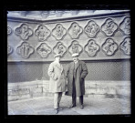 Deux hommes devant les bas-reliefs de soubassement de l'ébrasement côté gauche du portail central de la façade Ouest, dit Portail du Saint-Sauveur, de la Cathédrale d'Amiens (Somme)