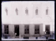 Professeur et enfants devant la porte et la fenêtre entrouverte de la façade d'une école.