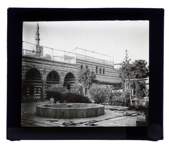 Cour intérieure à arcades et fontaine, plus loin un minaret.