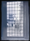 Vue d'un minaret à travers une fenêtre grillagée.