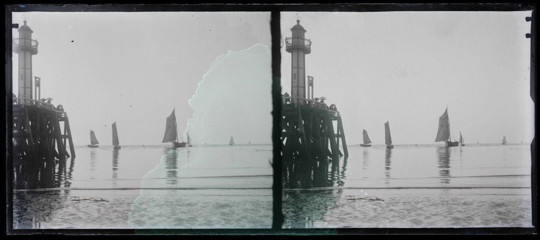 Phare en bout de jetée de port, au loin des bateaux de pêche.