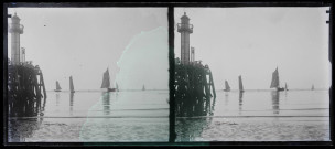 Phare en bout de jetée de port, au loin des bateaux de pêche.