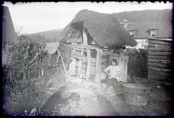 Jeune fille assise sur la margelle d'un puits d'une maison normande.