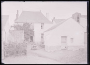 Jeunes enfants dans une brouette devant une habitation de bourgade.