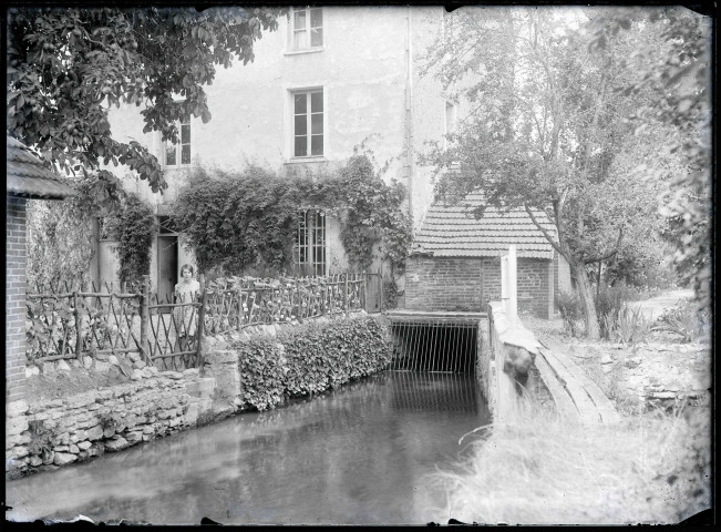 Jeune fille s'appuyant à une barrière séparant une habitation d'un cours d'eau.