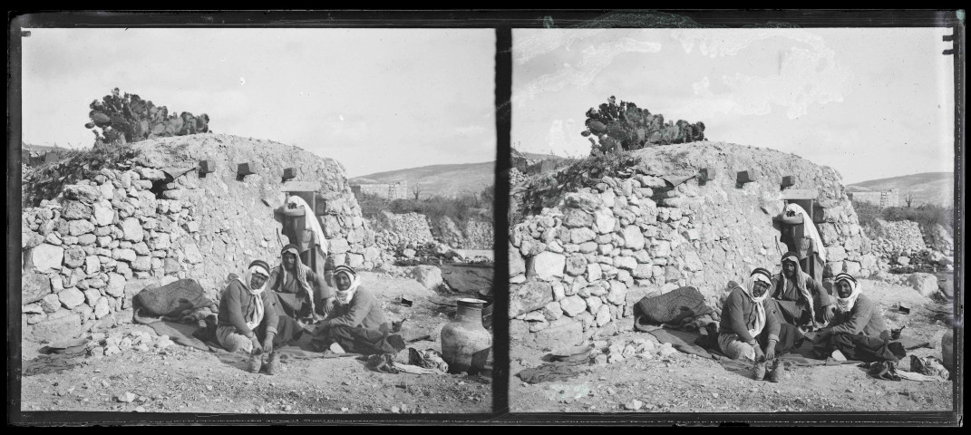 Hommes assis devant une habitation en pierre et en terre.