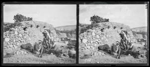 Hommes assis devant une habitation en pierre et en terre.