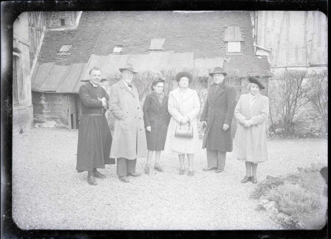 Hommes, femmes et prêtre posant dans la cour d'une habitation.