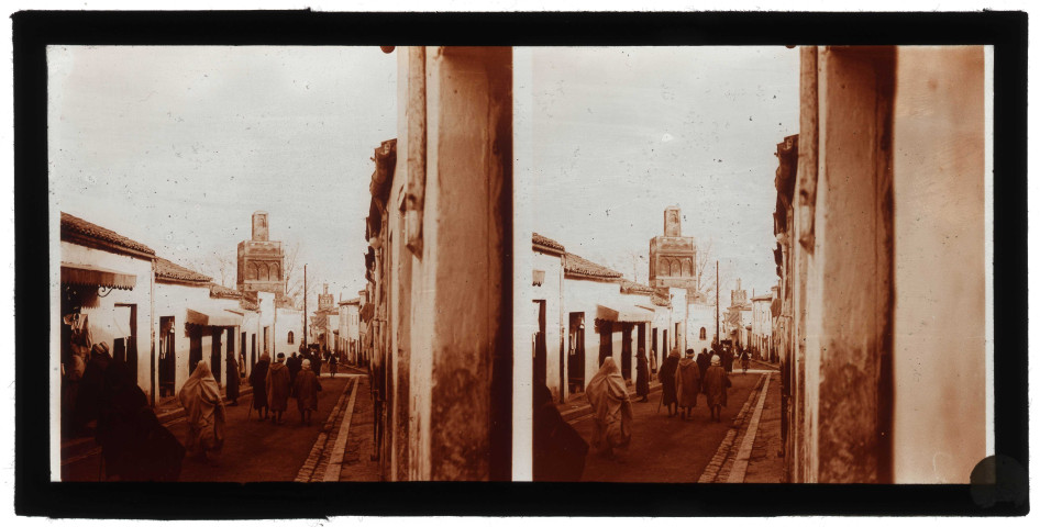 Bédouins dans les ruelles d'une ville d'Algérie, à l'arrière plan des minarets.