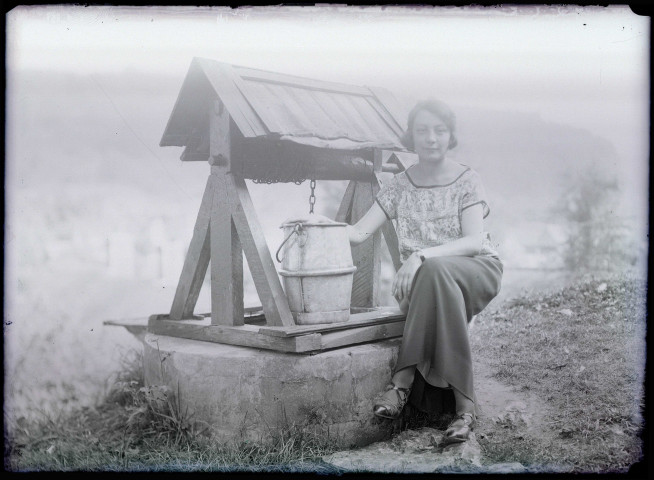 Portrait d'une femme assise sur la margelle d'un puits.