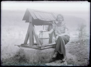 Portrait d'une femme assise sur la margelle d'un puits.