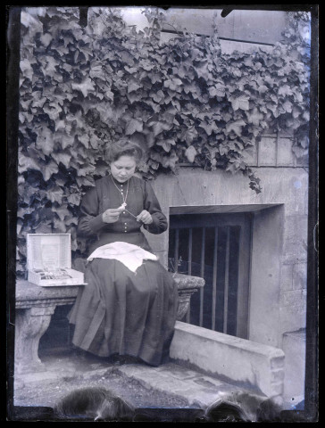 Femme à l'ouvrage sur un banc en pierre.