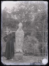 Jardin du presbytère de Saint-Aubin-du-Thenney (Eure), un prêtre (M. Machal) est appuyé contre la statue du Saint-Évêque.