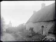 Chaumière et puits au bord d'un chemin menant à un village breton.