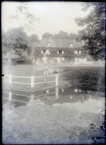 Petit garçon au bord d'une rivière près d'un manoir normand.