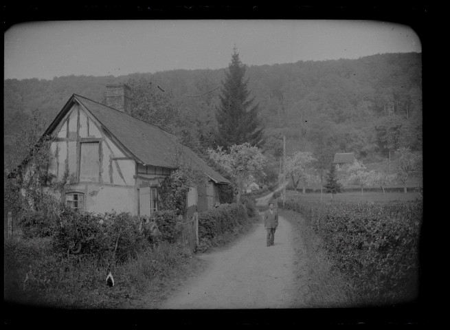 Portrait d'un homme sur une route bordée par une chaumière.