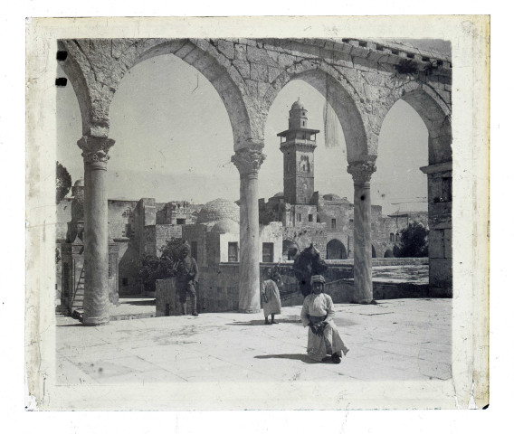 Militaire et enfants sur une place à arcades devant un minaret.