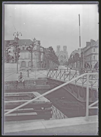 Vue d'un pont menant à une grande avenue commerçante, avec en perspective la cathédrale de Reims (Marne).