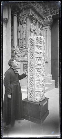 L'abbé Bretocq posant devant un fût de colonne octogonale en pierre portant les signes du zodiaques dans l'église abbatiale de Souvigny (Allier).