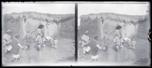 Hommes et enfants à un point d'eau devant une habitation en torchis.