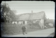 Femme et son chien sur un chemin devant une chaumière normande.