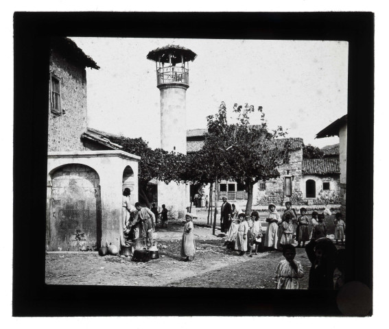 Enfants à la fontaine sur une place avec un minaret.