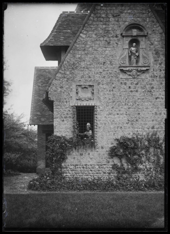 Femme en costume traditionnel normand à la fenêtre d'une habitation.