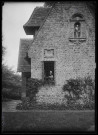 Femme en costume traditionnel normand à la fenêtre d'une habitation.