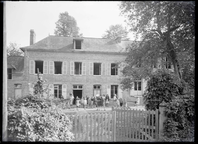 Enfants et sœurs à cornettes dans la cour d'une école de campagne.