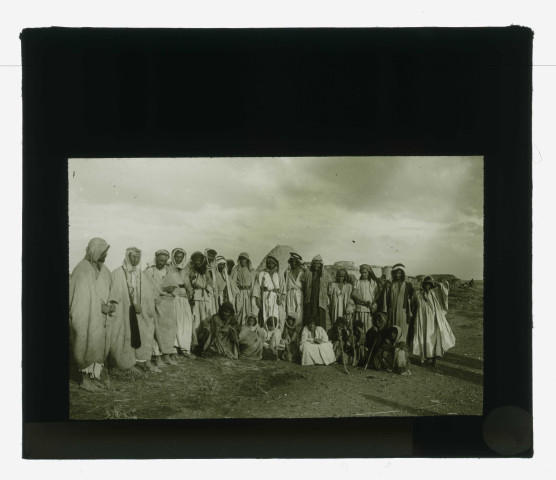 Groupe de bédouins devant des habitations en terre.
