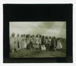Groupe de bédouins devant des habitations en terre.