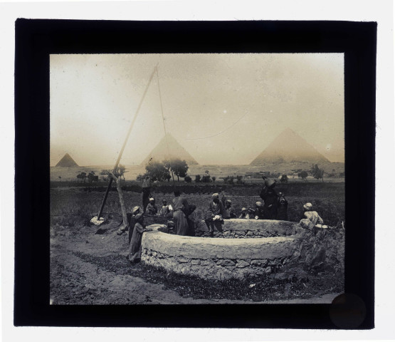 Bédouins et enfants au puits dans la campagne égyptienne, au loin les pyramides.