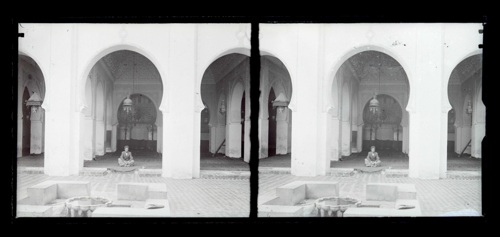Jeune garçon assis dans la cour intérieure à arcades et fontaine d'une habitation traditionnelle algérienne.