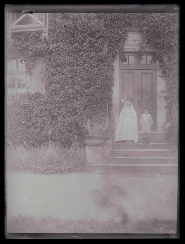 Communiante et jeune garçon sur le perron d'une habitation.