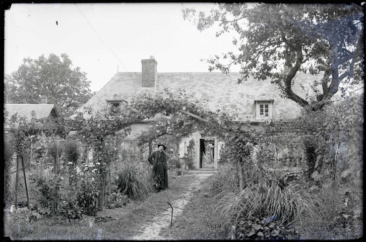 Curé dans un jardin devant une maison de la campagne normande.