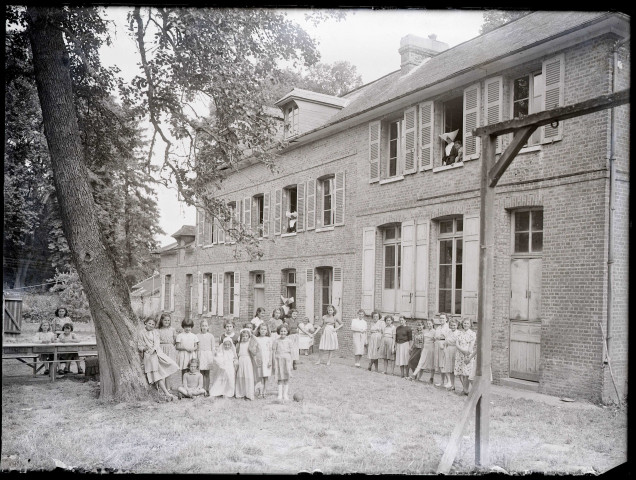 Enfants et sœurs à cornettes dans la cour d'une école de campagne.